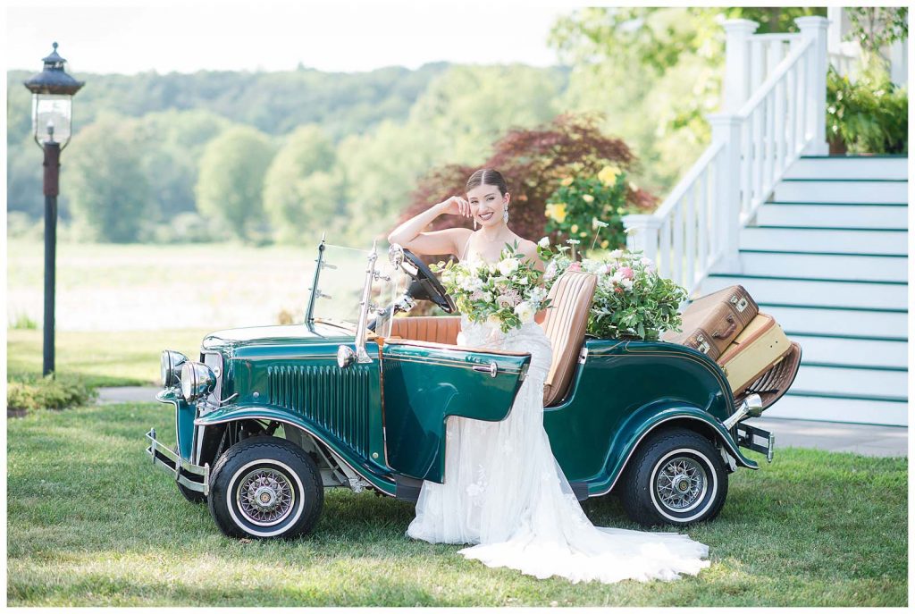 bridal portrait in classic car with vintage suitcases and stunning florals at new jersey venue