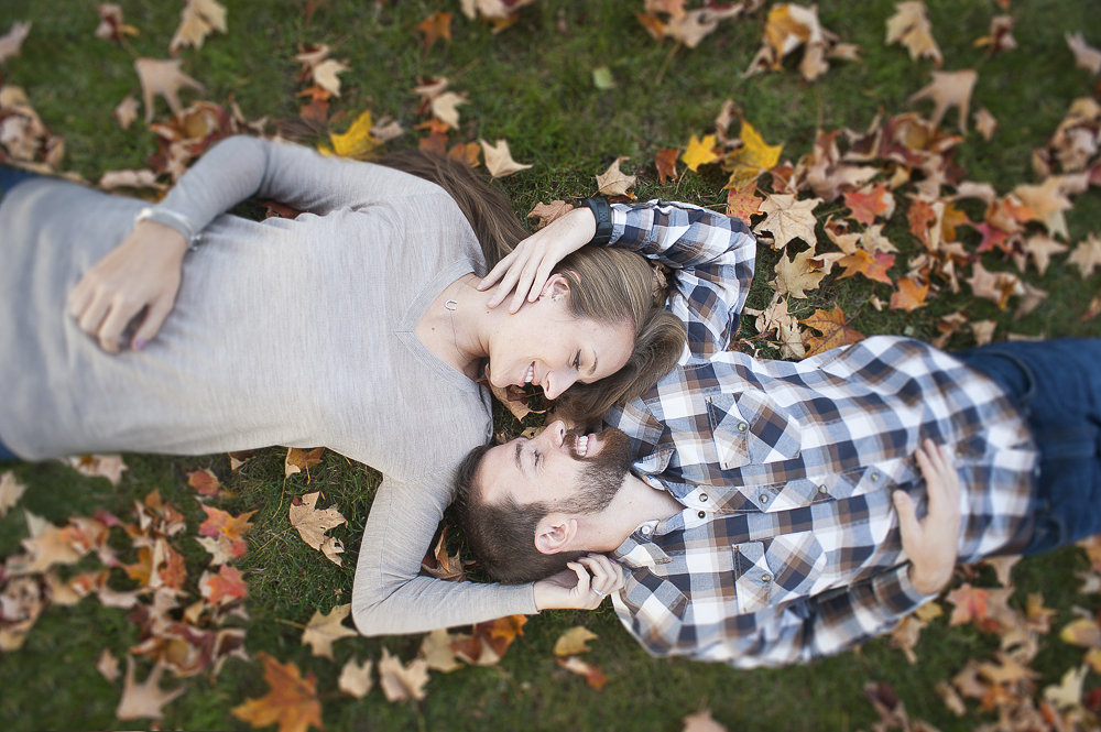 Portrait of the engaged couple during their engagement session laying in the leaves at Monmouth University.