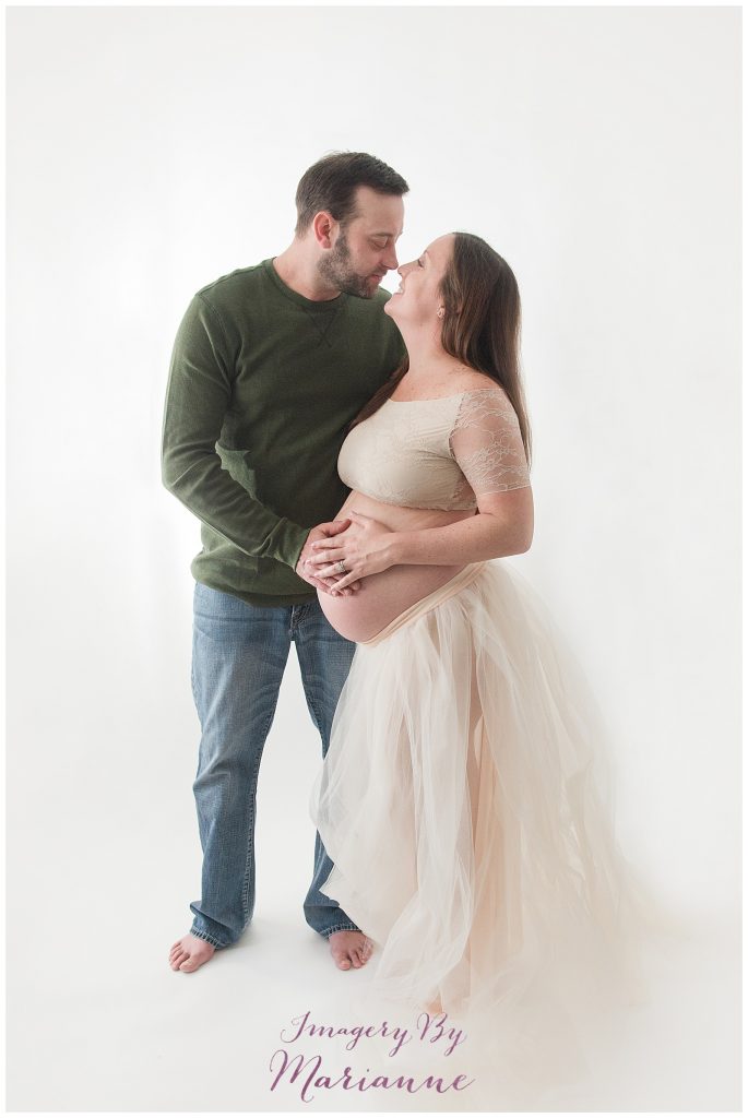 Expecting Mom and Dad hold exposed baby bump during studio photo session.